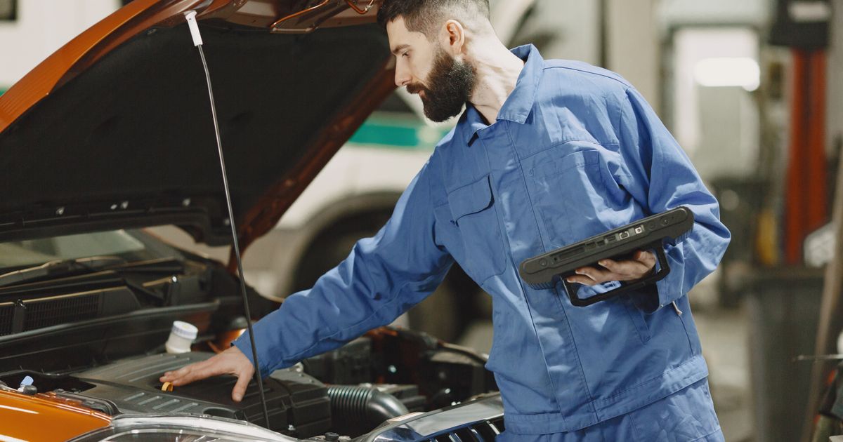 Mecánico revisando el motor de un carro con una tablet en la mano
