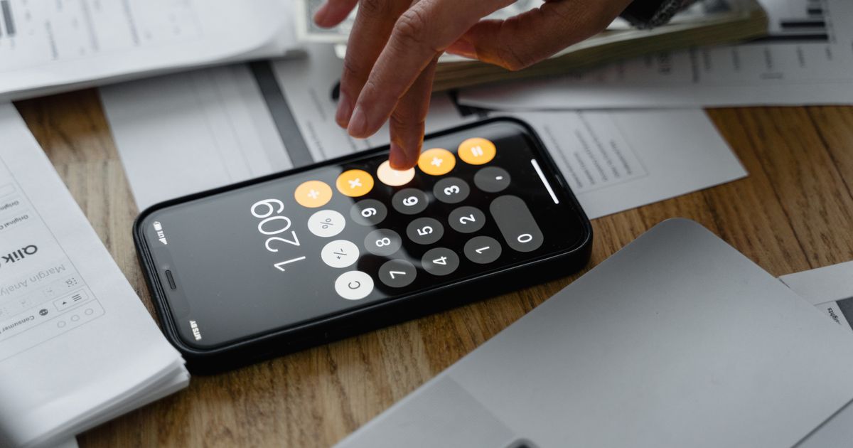 Mano usando la calculadora de un celular sobre un escritorio