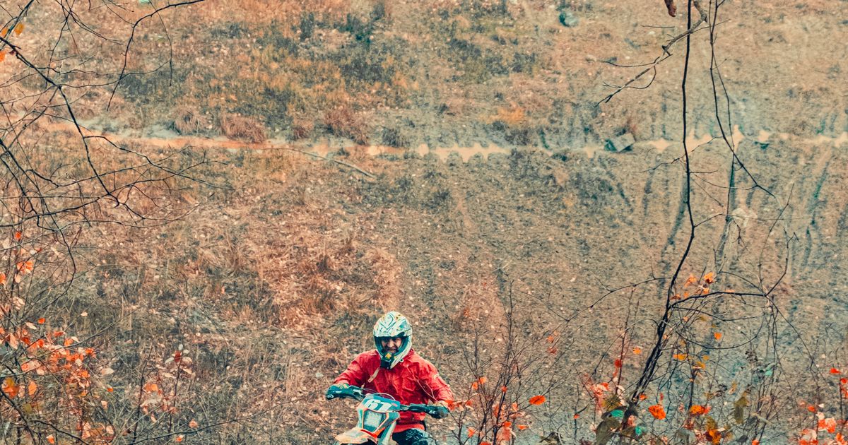 Motociclista de enduro cruzando un sendero de tierra en un bosque